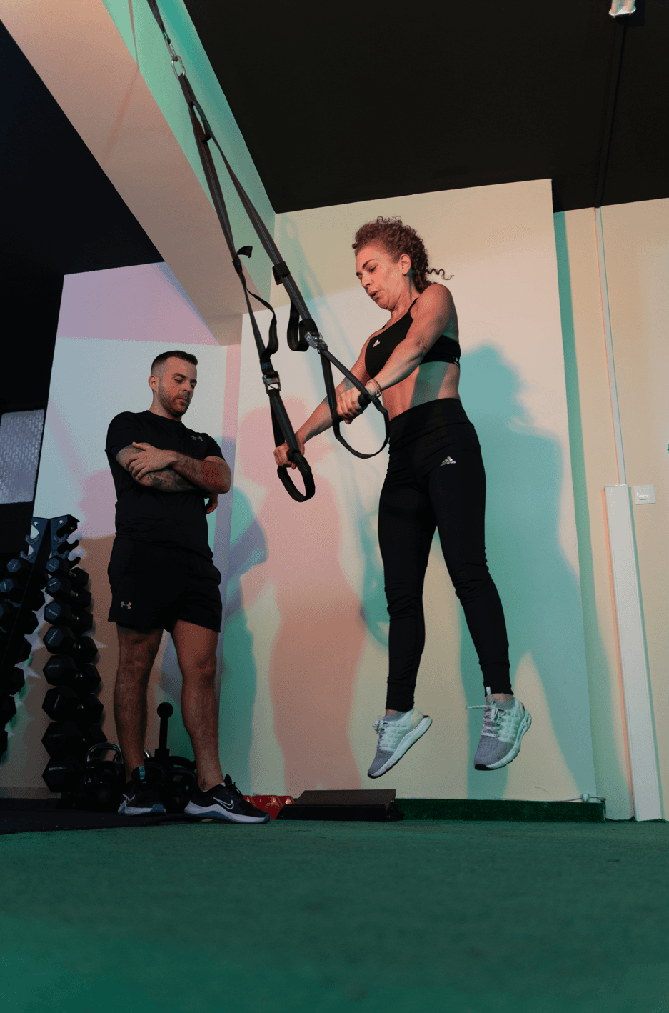 Αθλήτρια εκτελεί άσκηση με ιμάντες TRX υπό την επίβλεψη trainer